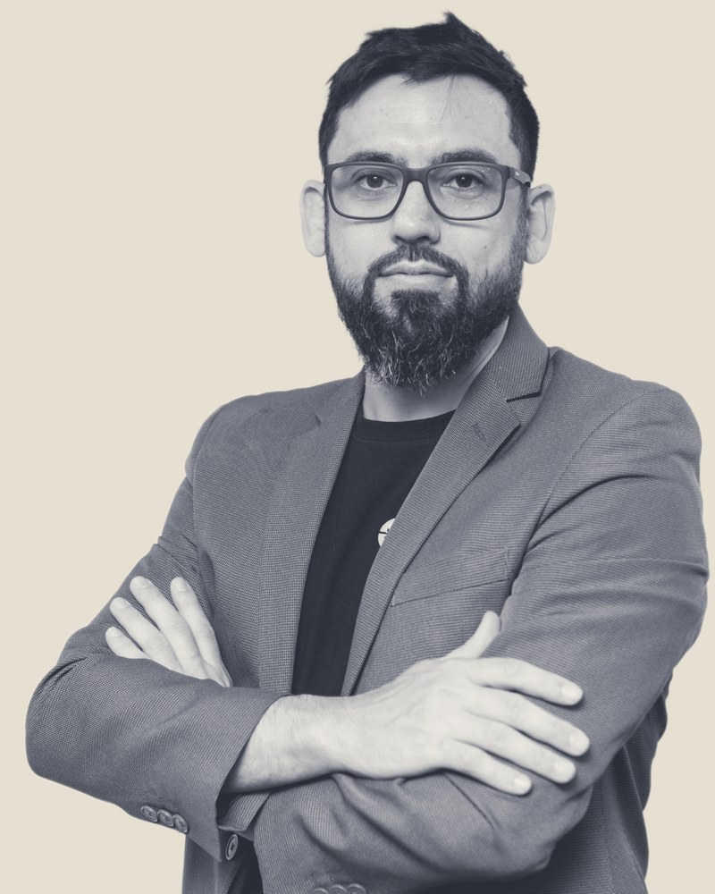 Retrato em preto e branco de Vavá Capelari, de óculos, barba e blazer, com os braços cruzados